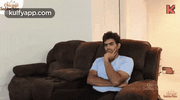 a man is sitting on a couch with his hand on his chin and the words kulfyapp.com on the bottom