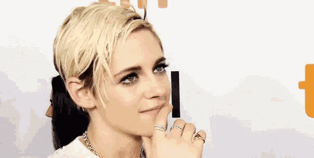 a woman with short blonde hair and a ring on her finger is smiling and covering her mouth with her hand .