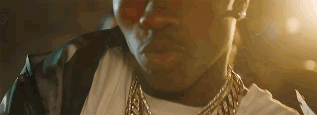 a close up of a man wearing a white shirt and a gold chain around his neck .