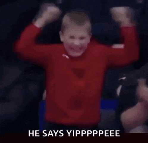 a young boy in a red shirt is raising his arms in the air and says he says yipppppee
