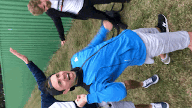 a man in a blue jacket is standing in the grass with his arms in the air