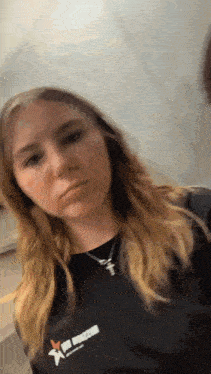 a woman wearing a black shirt with a cross on it is making a funny face