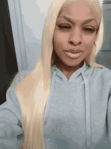 a woman with long blonde hair is wearing a gray hoodie