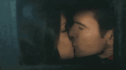 a man and a woman are kissing in a dark room behind a window .