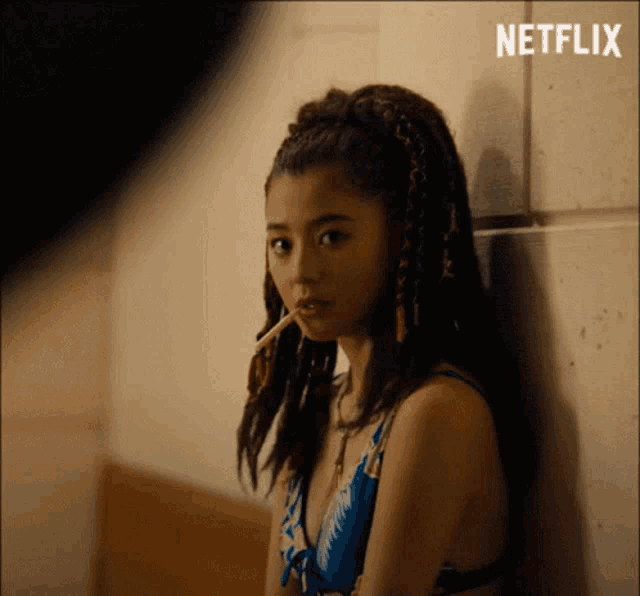 a woman leaning against a wall with a cigarette in her mouth and a netflix logo behind her