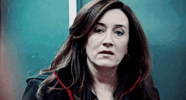 a woman in a black jacket with a red collar is looking at the camera .