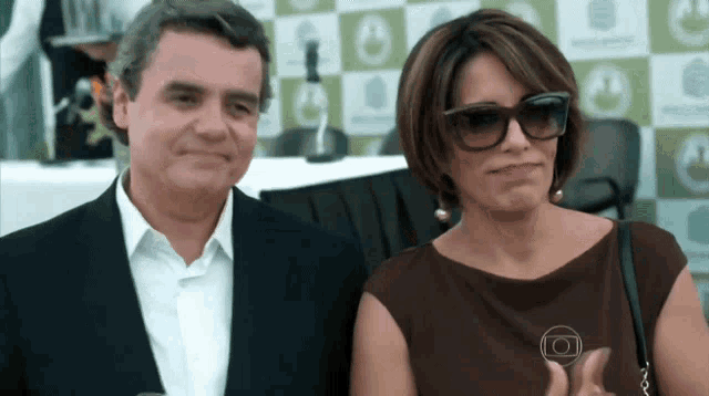 a man and a woman wearing sunglasses are standing next to each other in front of a green and white checkered background