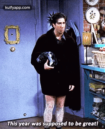 a man is standing in front of a door holding a dog and says this year was supposed to be great .
