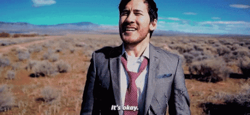 a man in a suit and tie is standing in a field and saying it 's okay