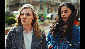 two women are standing next to each other on a city street . one of the women is wearing a denim jacket .