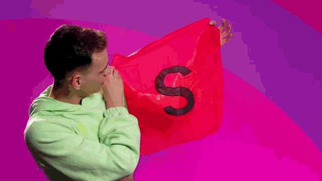 a man in a green sweatshirt is holding a red cloth with the letter s painted on it