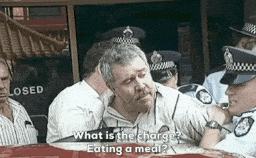 a group of police officers are standing around a man asking him what is the charge eating a meal