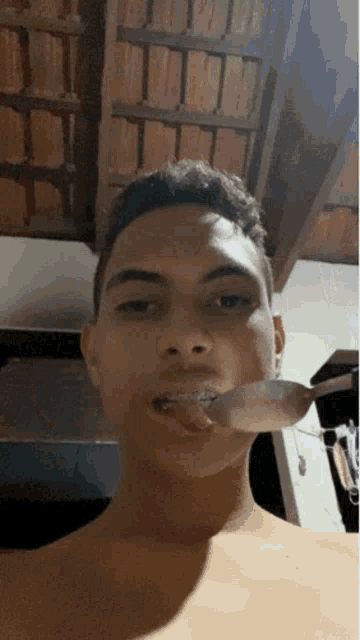 a shirtless young man is holding a spoon in his mouth