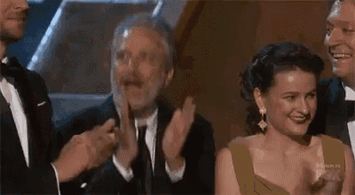 a group of people are applauding a woman in a yellow dress at an awards ceremony .