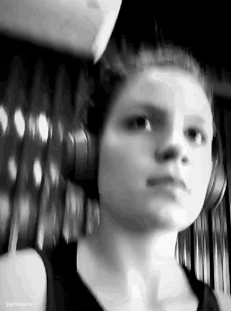 a black and white photo of a woman wearing headphones and looking at the camera .