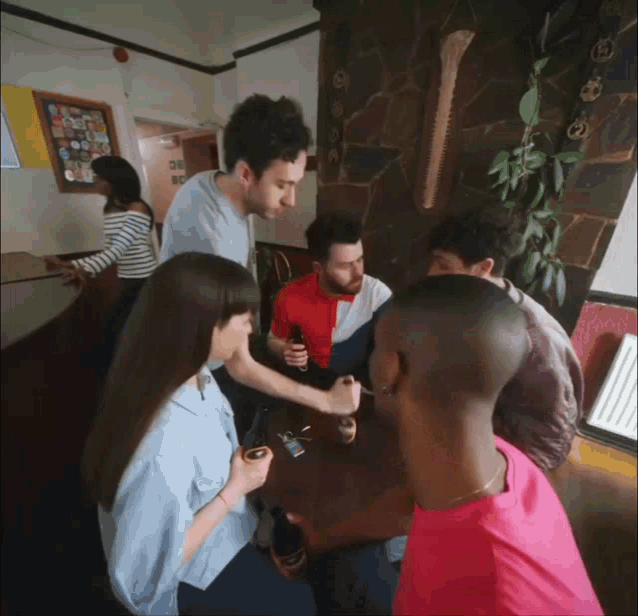 a group of people are gathered around a table with a man in a red shirt