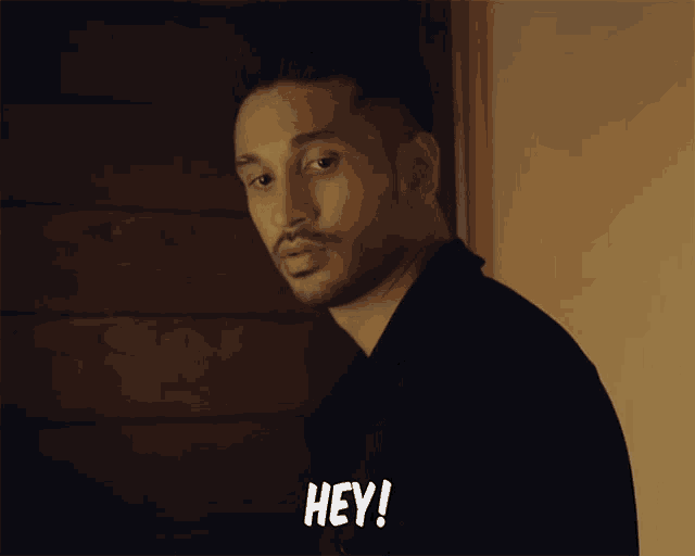 a man with a beard says hey in a dark room