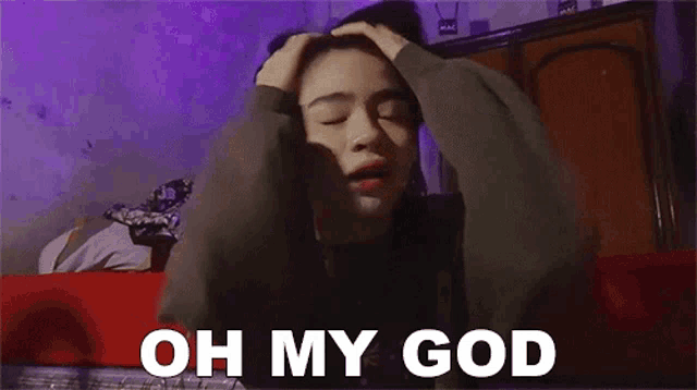 a woman is sitting on a couch with her hands on her head and the words `` oh my god '' written on the bottom .