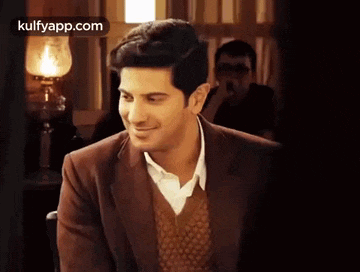 a man in a suit and sweater is smiling while sitting in a restaurant .