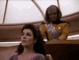 a woman in a purple dress sits in front of a man in a yellow uniform