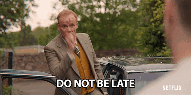 a man in a suit is getting out of a car and says " do not be late "