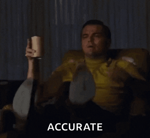a man in a yellow shirt is sitting on a couch holding a cup and pointing at something .