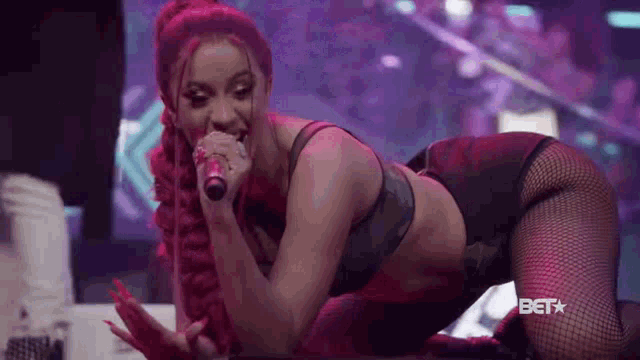 a woman in a bra and fishnet stockings is kneeling down and singing into a microphone on a stage .