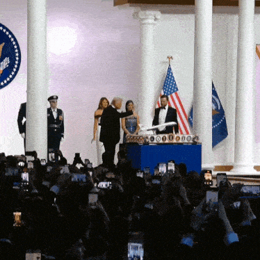 a man in a tuxedo stands in front of a crowd of people taking pictures of him