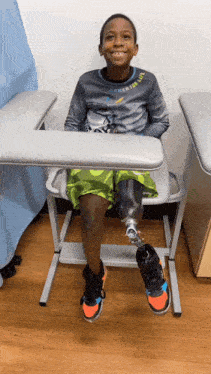 a young boy with a prosthetic leg is sitting at a desk and smiling