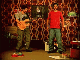 a man in a red shirt is playing a guitar next to another man in a grey shirt