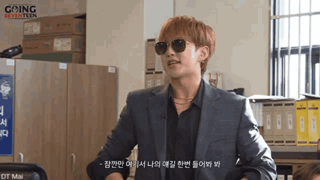 a man wearing sunglasses and a suit is standing in front of a window in an office .