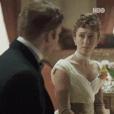 a man in a tuxedo and a woman in a white dress are looking at each other with the hbo logo in the corner