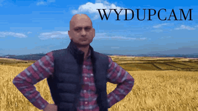 a man in a plaid shirt stands in front of a field with the words wydupcam written above him