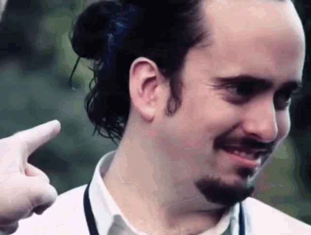 a man with long hair and a beard is smiling and pointing at someone