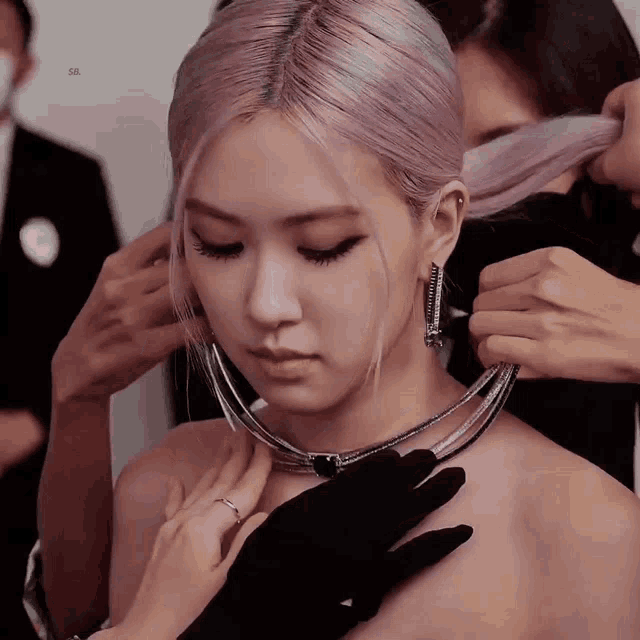 a woman with pink hair is being helped by a woman with black gloves