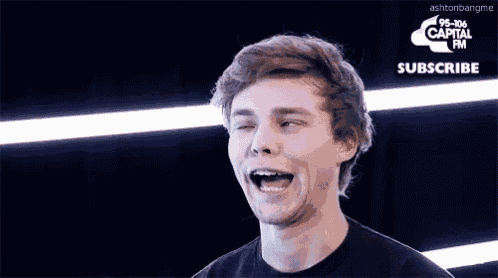 a young man in a black shirt is making a funny face in front of a sign that says 95-106 capital fm