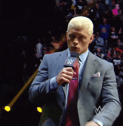 a man in a suit and tie is holding a microphone with a w on it