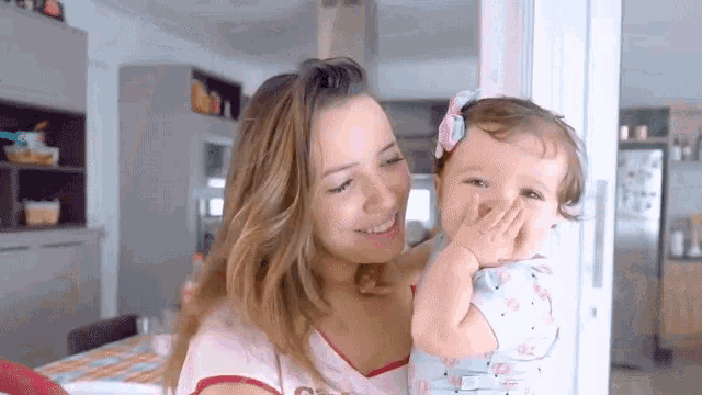 a woman is holding a baby in her arms and the baby is covering her mouth