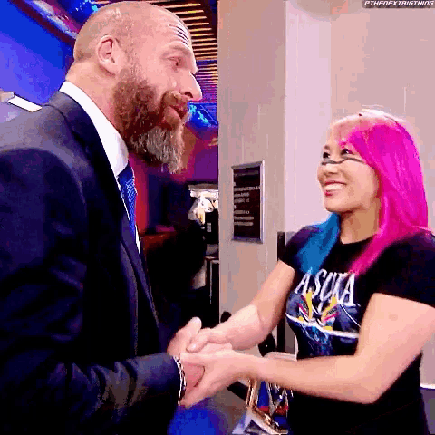 a man in a suit and tie shakes hands with a woman with pink hair wearing a shirt that says asuka