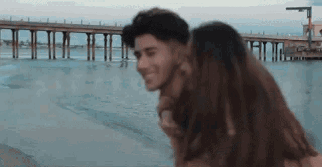 a man is giving a woman a piggyback ride on the beach in front of a pier .