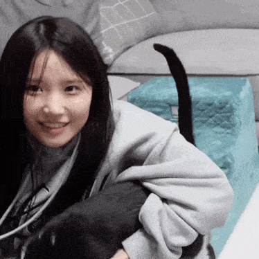 a girl in a grey sweatshirt holds a black cat in her arms