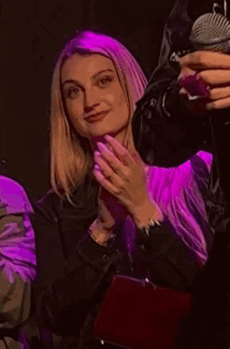 a woman is clapping her hands in front of a microphone in a dark room with purple lights .