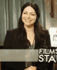 a woman is smiling while sitting at a desk in front of a sign that says `` films station '' .