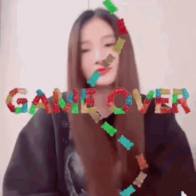 a girl with long hair is surrounded by gummy bears and the word game over is written in gummy bears .