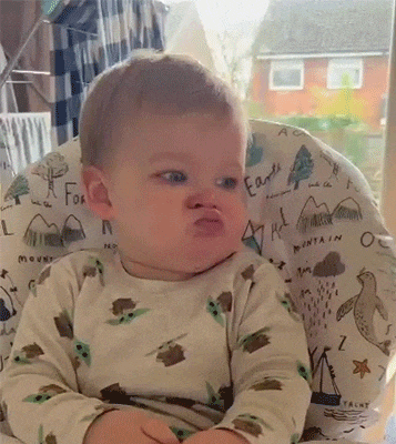 a baby is sitting in a high chair making a funny face .