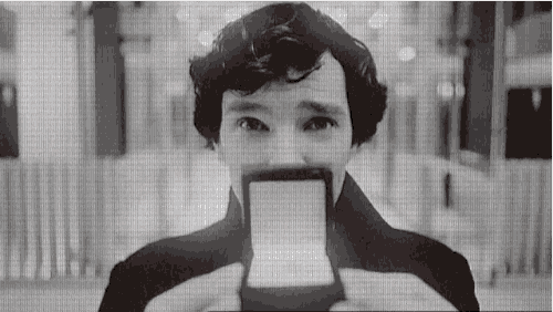 a man is holding a piece of paper in front of his face and looking at it .