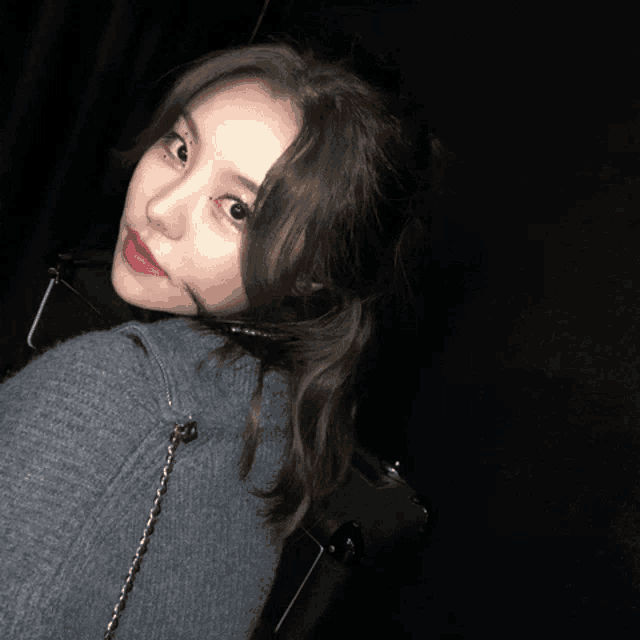 a woman wearing a gray sweater and red lipstick looks over her shoulder