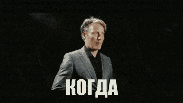 a man in a suit is looking at his watch with the word когда in white letters on the bottom