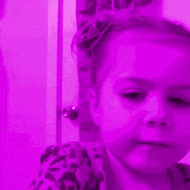 a child 's face is lit up in purple with a light behind it