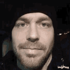 a close up of a man 's face with a beard wearing a black hat .